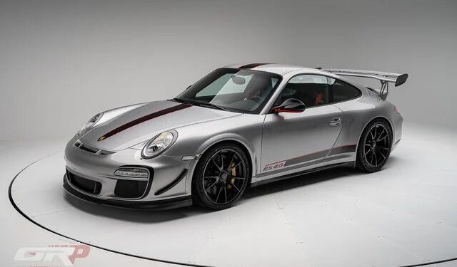 An ultra-rare silver PTS 911 GT3 RS 4.0 sports car with black and red racing stripes, black wheels, and a large rear wing, displayed in a well-lit studio setting by Graham Rahal Performance.