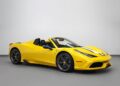 A yellow Ferrari 458 Speciale convertible with black and white racing stripes is parked indoors against a plain white wall, showcasing why it’s among the best modern Ferraris.