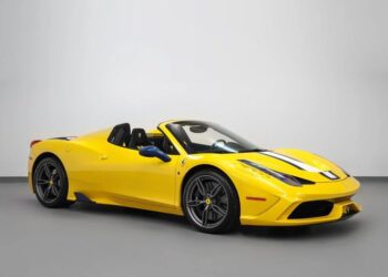 A yellow Ferrari 458 Speciale convertible with black and white racing stripes is parked indoors against a plain white wall, showcasing why it’s among the best modern Ferraris.