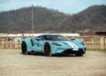A sleek, blue Lamborghini Diablo VT 6.0 with a white stripe is parked on a gravel surface, set against a backdrop of rolling hills and a cloudy sky, reminiscent of the elite offerings often seen at Broad Arrow Auctions.
