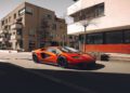 A sleek red Lamborghini Diablo VT 6.0 is parked on a street in a residential area, modern buildings standing proudly in the background, as if waiting for its moment under the Broad Arrow Auctions spotlight.