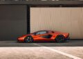 A sleek, orange Lamborghini Diablo VT 6.0 sports car is parked in front of a modern, gray and beige wall.