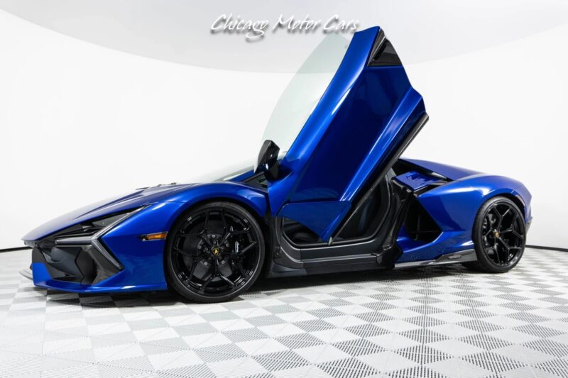 A blue Lamborghini Revuelto with scissor doors open is displayed in a showroom with a patterned floor, showcasing the elegance of supercars.