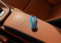 A Riviera Blue car key fob rests elegantly on the tan leather seat of a Porsche 911, ready for its next adventure.