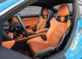 For sale: A striking Riviera Blue Porsche 911 with its door ajar, revealing an interior of vibrant orange racing-style seats, sleek black trim, and a modern dashboard design.