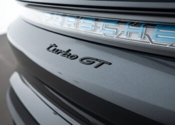 Close-up of the rear badge on a luxury car, highlighting the "turbo GT" badge and part of the illuminated "Porsche" emblem on a metallic gray surface.