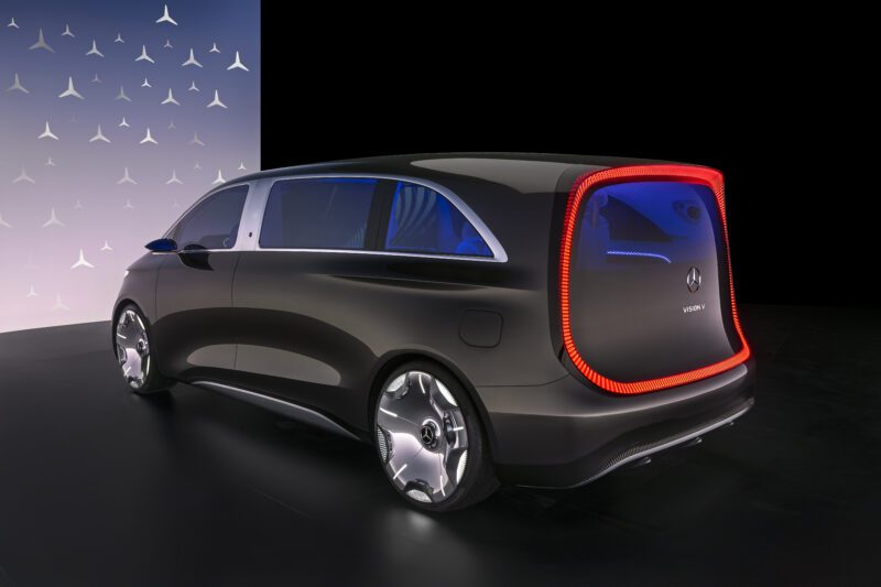 The Mercedes-Benz Vision V luxury Sprinter van boasts a sleek black exterior, illuminated rear light frame, and large silver wheels, all showcased under striking studio lighting.