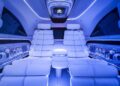 Interior of a Mercedes-Benz Vision V Sprinter ultra-luxury van with white leather reclined seats, blue LED lighting, and built-in cup holders along both sides.