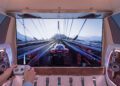 A person plays a racing video game on a large screen inside an ultra-luxury Mercedes-Benz Sprinter Van, holding a game controller.