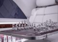 A luxury chess set with silver pieces is displayed on a fold-out table inside a Vision V Mercedes-Benz Sprinter van with white leather seats.
