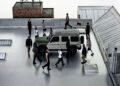 A group of people clad in Moncler jackets stroll around a parked Mercedes-Benz SUV on a rooftop, with a water tower emblazoned in the background.