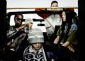 Five people in casual streetwear sit inside a Mercedes-Benz, sporting a mix of hats, hoodies, and sunglasses. Among them, one wears a Moncler jacket. The vehicle has a sleek design with a visible yellow roll bar.