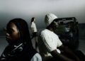 Three fashionably dressed individuals pose with a Mercedes-Benz off-road vehicle against a foggy backdrop.