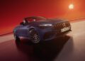 A blue Mercedes-AMG convertible car is parked on a surface with a fiery orange sky and a low sun in the background. This limited-edition model showcases a sleek design with a prominent front grille and alloy wheels.