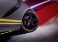 Close-up of a Mercedes-AMG's rear wheel with a black multi-spoke rim and Pirelli tire. The limited-edition car flaunts a gray body with yellow stripes, against a blurred red and white backdrop that suggests speed or motion.