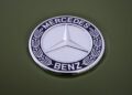 Close-up of a silver Mercedes-Benz emblem with the iconic three-pointed star logo on a green new Mercedes-Benz G-Class, showcasing a design STRONGER THAN THE 1980s.