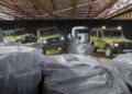 Three green Mercedes-Benz G-Class SUVs are displayed indoors among artificial rocks, with a large letter "G" and black curtains in the background—a new unveiling showcasing a model that's STRONGER THAN THE 1980s.