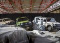 Three new G-Class SUVs in beige, green, and white are displayed indoors among artificial rocks, with a black curtain and red steel beams in the background—showcasing that they're STRONGER THAN THE 1980s.