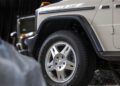 Close-up of the front wheel and fender of a beige Mercedes-Benz G-Class SUV parked outdoors, with part of another vehicle visible in the background—this new 1-of-460 edition is STRONGER THAN THE 1980s.