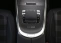 Close-up of a Mercedes-Benz G-Class center console with control buttons, a touchpad, and the exclusive "1-of-460" inscription on a wood-finish surface between two plaid-patterned seats—STRONGER THAN THE 1980s.