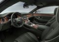 The luxurious interior of this Bentley features dark green leather seats and elegant wood trim. A high-tech dashboard complements the round air vents, while the steering wheel proudly displays the iconic emblem visible in models like the Continental GT and Flying Spur.