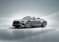 A sleek silver convertible sports car, reminiscent of a Bentley Continental GT, is showcased with its headlights gleaming against a gray background.
