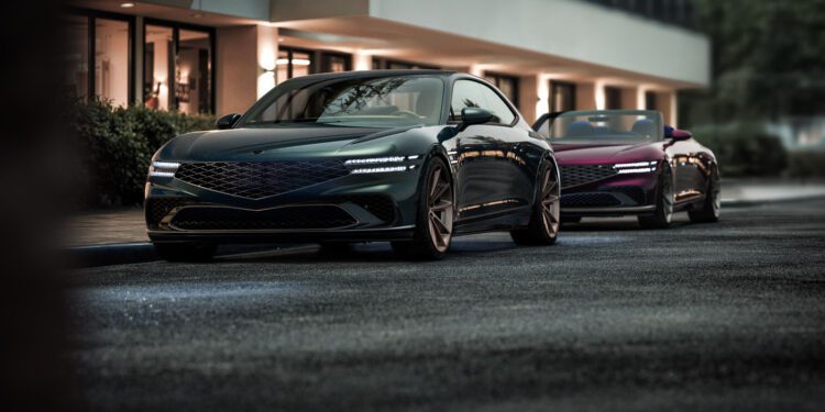 Two sleek, modern vehicles, including a Genesis X Gran Coupe with angular designs and illuminated headlights, stand parked on a city street in front of a building boasting large windows.