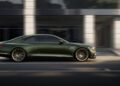 A sleek Genesis X Gran Coupe glides down the city street, its luxurious green finish gleaming against the backdrop of blurred modern buildings.