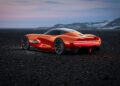 A sleek, red futuristic Genesis concept car with a smooth, aerodynamic design is parked on a rocky terrain with a mountainous backdrop at dusk.
