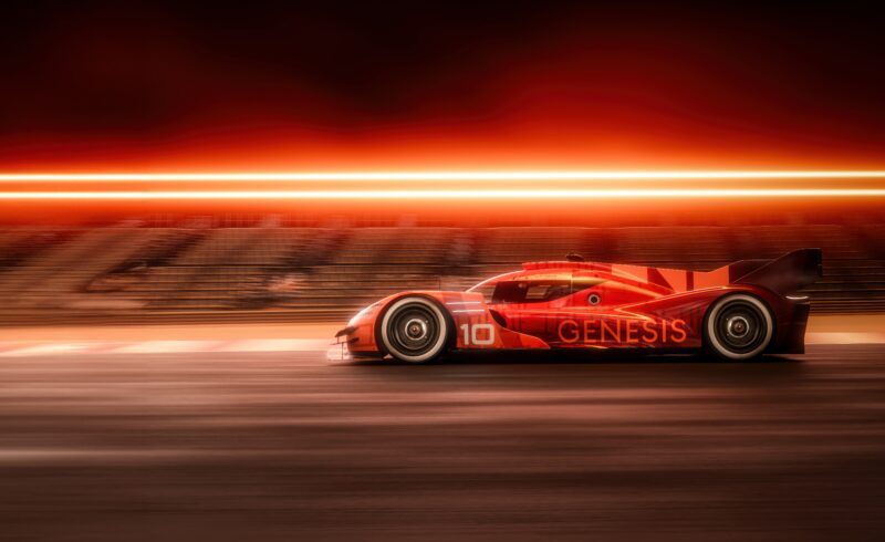 A red Genesis GMR-001 Hypercar with the number 10 on the side speeds along a track, motion blur and bright orange lights in the background, evoking excitement reminiscent of the New York International Auto Show.