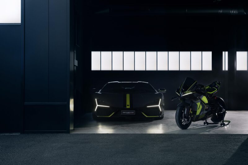 A sleek black Lamborghini and a matching Panigale V4 motorcycle with neon accents are parked in a dimly lit garage next to a large window.