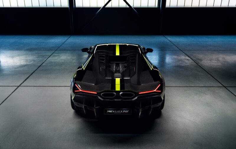 A sleek black sports car with a yellow stripe down the center, its rear and taillights glowing in the dimly lit garage, exudes an allure reminiscent of a Revuelto.