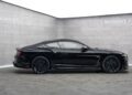 A black Bentley Continental GT with Mansory customizations is displayed in a minimalist showroom with gray walls and "MANSORY" branding.
