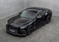 A black Bentley Continental GT luxury sports coupe with Mansory customizations and a carbon fiber finish is parked indoors on a gray tiled floor, viewed from a high angle.