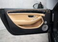 The image shows the interior of a luxury car door with beige leather, chrome accents, a wood trim, speaker, and control buttons.