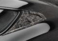 Close-up of a car’s rear side window and pillar, featuring a carbon fiber trim with a Maserati logo badge, showcasing premium customizations reminiscent of those seen on a Bentley Continental GT or Mansory edition.