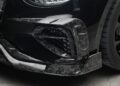 Close-up of a Bentley Continental GT's front bumper with a carbon fiber splitter and detailed air vents, featuring the Mansory logo and customizations.