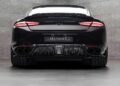 Rear view of a Bentley Continental GT modified by Mansory, featuring customizations like wide tires, quad exhausts, and LED tail lights, set against a gray tiled wall.
