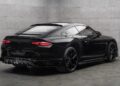 A black Bentley Continental GT with striking Mansory customizations is parked in a minimalist, gray concrete room, viewed from the rear side angle.