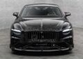 Front view of a Bentley Continental GT with Mansory customizations, featuring a carbon fiber hood and trim, large front grille, and sleek headlights in a gray showroom.