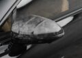 Close-up of a car’s side mirror with a distinct textured, patterned cover—an eye-catching customization on a black Bentley Continental GT.