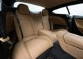 The image shows the interior of a luxury car with tan leather seats, detailed stitching, and sleek black and wood trim accents.