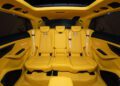 The image shows the luxurious yellow leather interior and seating of the rear compartment in a high-end SUV, featuring detailed stitching, ambient lighting, and Mansory customizations.