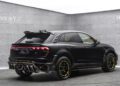 A matte black Mansory luxury SUV with yellow accents and bold sporty customizations is parked indoors against gray paneled walls.