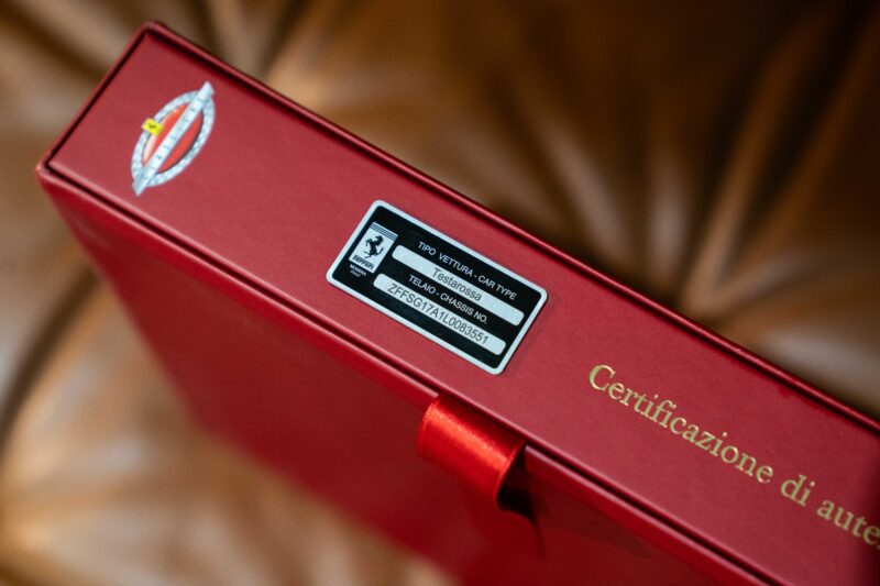 A close-up of a red box with a certification label and the words "Certificazione di autenticità" printed in gold on the side, hinting at its connection to a rare car like the iconic 1990 Ferrari Testarossa.