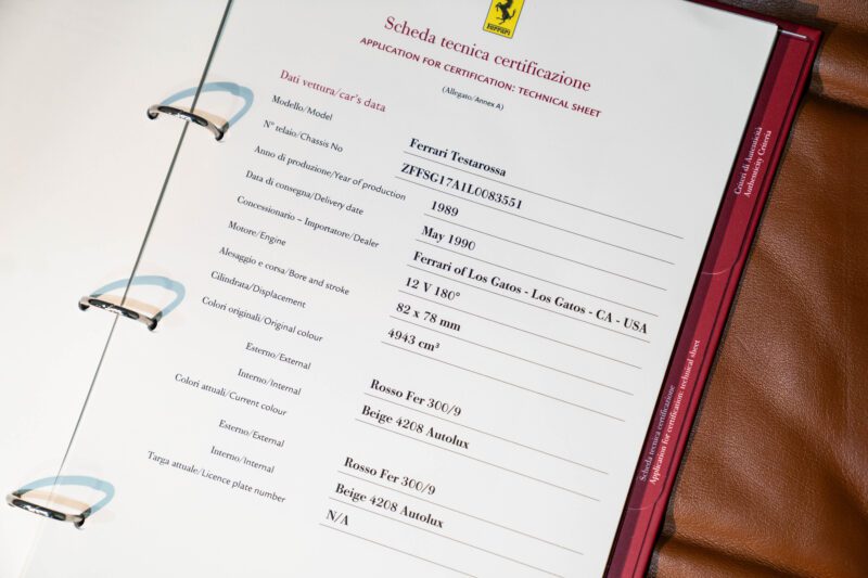 A close-up of a rare Ferrari technical certification sheet in a binder, showing vehicle details such as model, year, chassis number, and original color information.