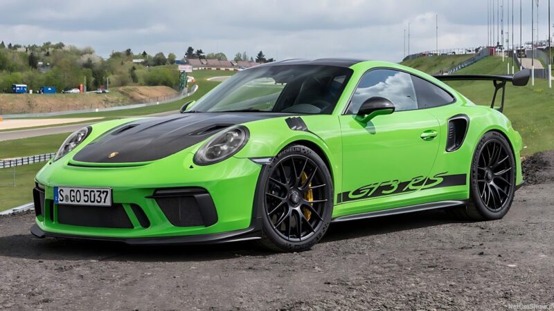 A striking Porsche 911 GT3 RS in bright green is parked outdoors near a racetrack on a cloudy day.