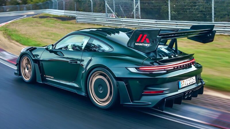 A green Porsche 911 GT3 RS with a large rear wing drives on a racetrack, featuring aerodynamic upgrades and "Manthey" branding.