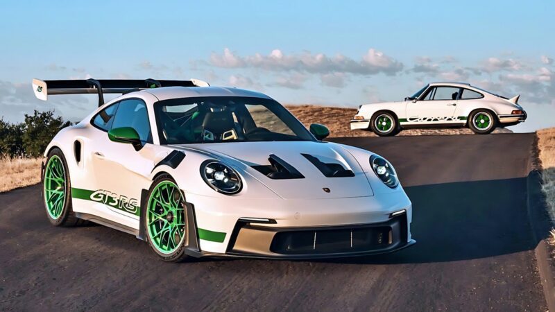Two white Porsche sports cars, including a Porsche 911 GT3 RS with green accents, are parked on a paved road—the modern model in the foreground and the classic in the background.
