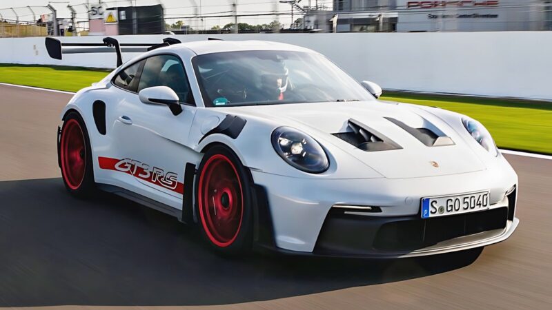 A Porsche 911 GT3 RS with striking red wheels and a large rear wing speeds along the racetrack, showcasing the iconic sports car’s racing pedigree.